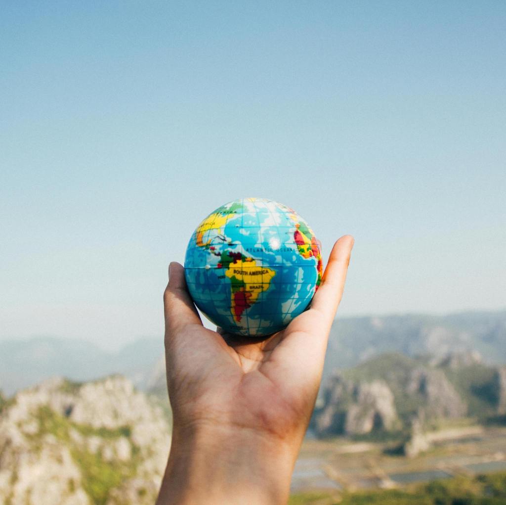 Hand holding a miniature globe in an outdoor travel setting, symbolising global group trips
